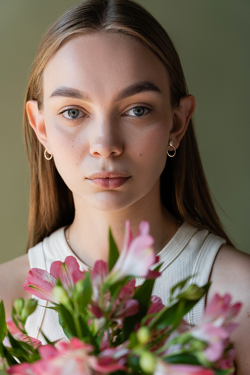 portrait of woman with natural makeup near blurred alstroemeria flowers isolated on green