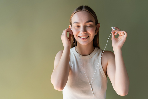 cheerful woman with closed eyes and wired earphones isolated on green