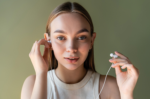 young woman with wired earphones looking at camera isolated on green