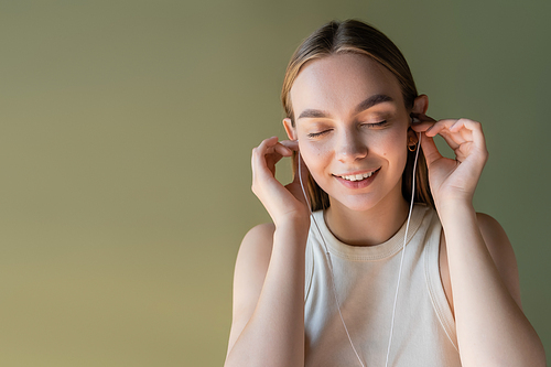 joyful woman with closed eyes listening music in wired earphones isolated on green
