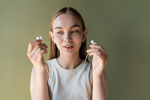 young woman in white tank top holding wired earphones isolated on green