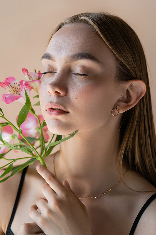 sensual woman with closed eyes and perfect skin smelling alstroemeria flowers isolated on beige