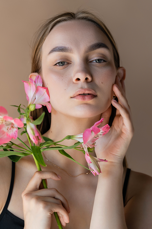 sensual woman with branch of alstroemeria touching cheek isolated on beige