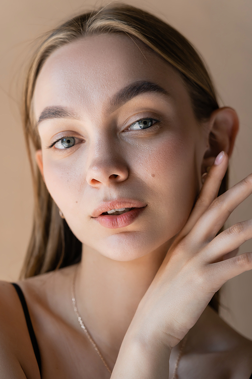 portrait of woman with natural makeup and hand near perfect face isolated on beige