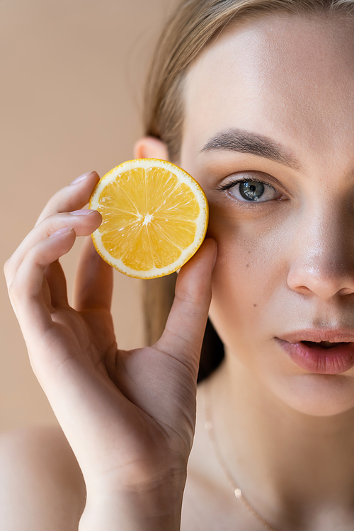 cropped view of woman with natural makeup holding half lemon isolated on beige