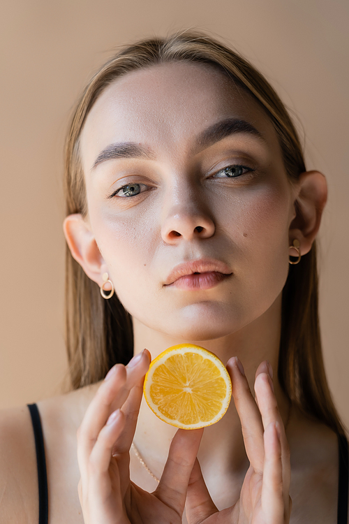 portrait of pretty young woman with perfect skin holding half lemon isolated on beige