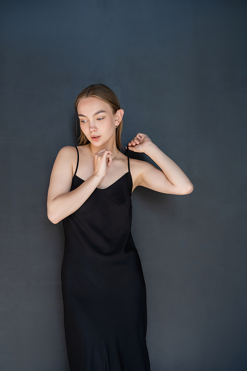 sensual woman touching strap of black dress on dark background