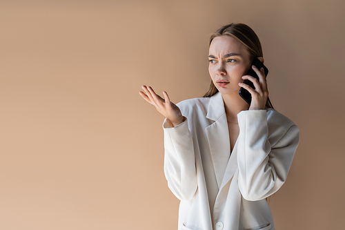 displeased woman talking on cellphone and pointing with hand isolated on beige