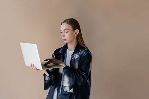 woman in trendy gradient shirt using laptop isolated on beige