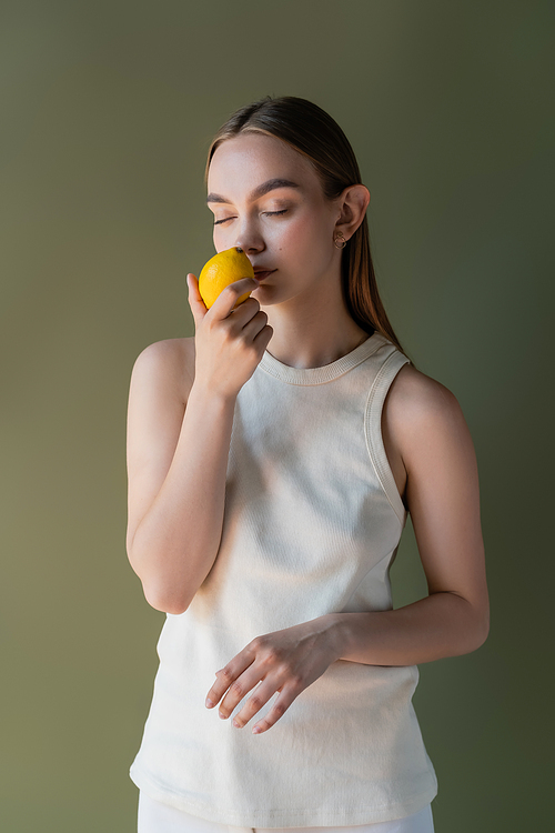 woman in white tank top smelling aromatic lemon with closed eyes isolated on green