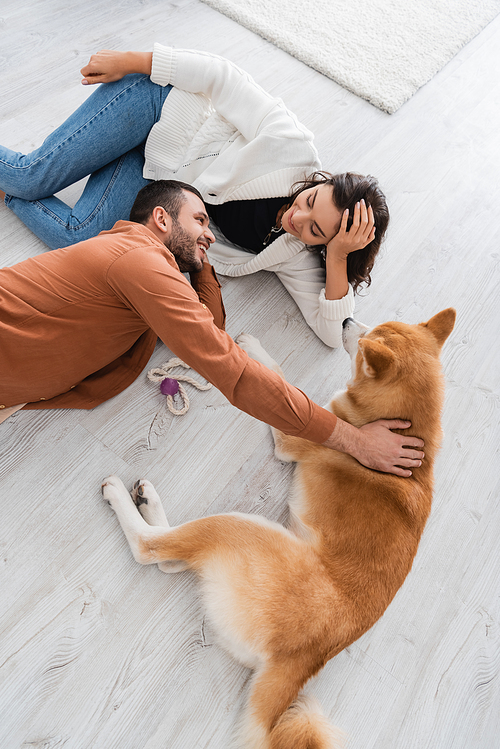 top view of happy young couple looking at each other while lying of floor with akita inu dog