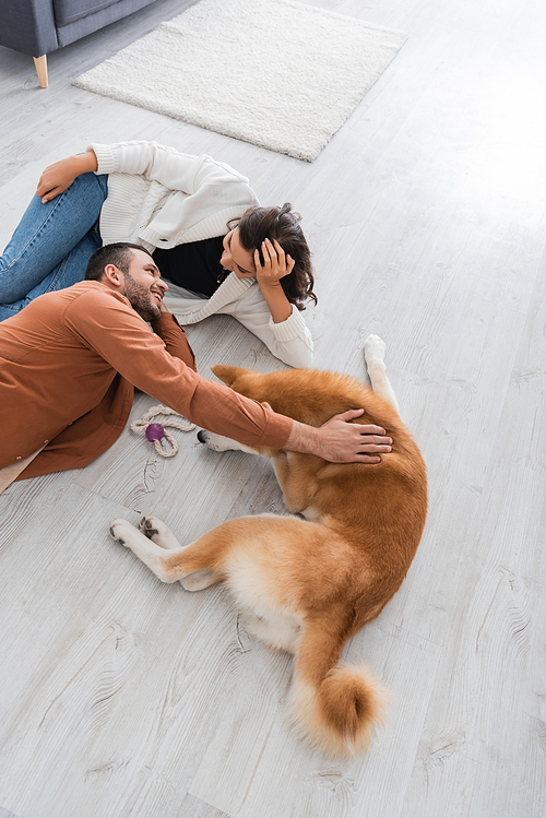 top view of joyful young couple looking at each other while lying of floor with akita inu dog