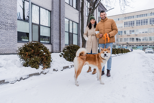 happy man holding leash while walking with girlfriend and akita inu dog