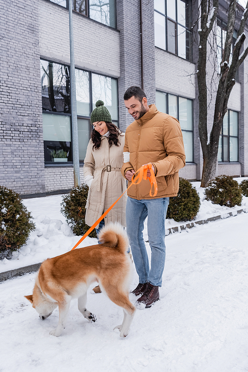 cheerful man holding leash while walking with girlfriend and akita inu dog
