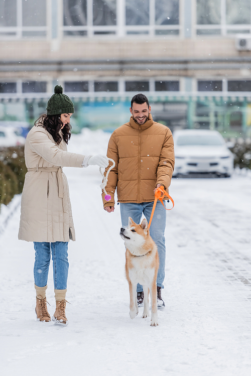 happy man holding leash while walking near girlfriend playing with akita inu dog