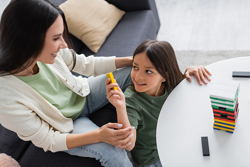 top view of happy babysitter playing wooden tower game with positive girl in living room