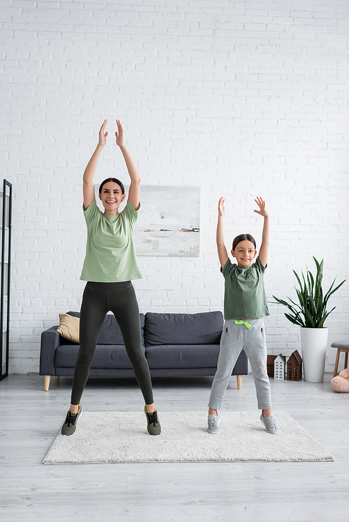 happy girl and nanny stretching on tiptoes with raised hands in living room