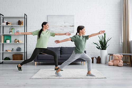 smiling child and babysitter training in warrior pose in modern living room