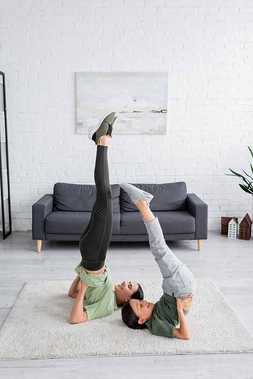 happy girl with babysitter training in supported shoulder stand pose on carpet in living room