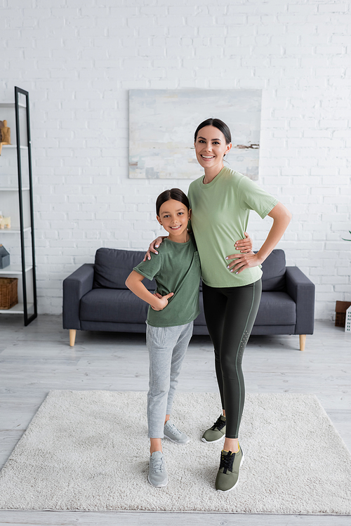 full length of happy nanny and child in sportswear embracing and looking at camera