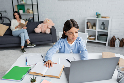 girl doing homework near computer and nanny sitting with book on blurred background