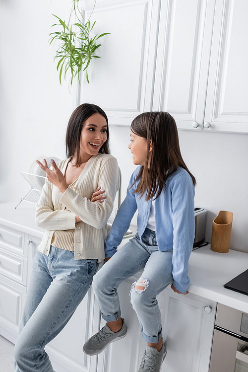 cheerful nanny talking to girl sitting on worktop in kitchen