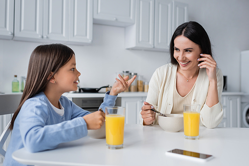 girl talking to happy nanny near bowls with breakfast and fresh orange juice