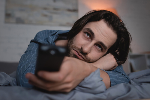Sleepless man with remote controller watching tv in bedroom