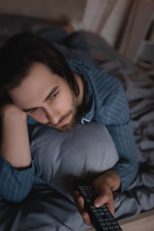 Bearded man clicking channels while lying on bed at night