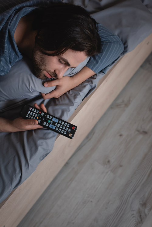 High angle view of man holding remote controller while sleeping on bed at night