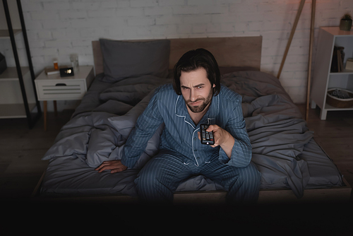 Displeased man with insomnia watching movie in bedroom at night