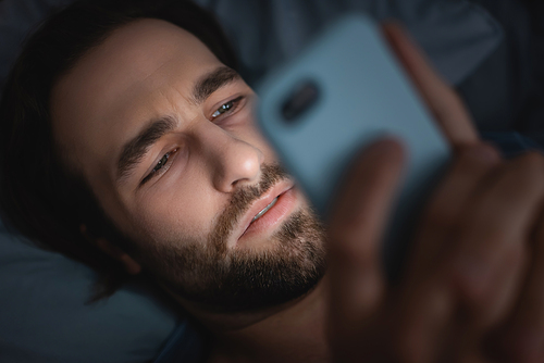 Top view of tired man using smartphone on bed at night