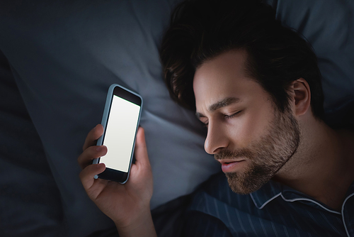 Top view of man in pajama holding smartphone with blank screen while sleeping on bed