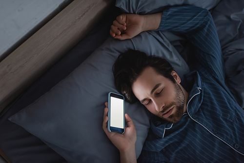 Top view of young man holding smartphone with blank screen while sleeping at home