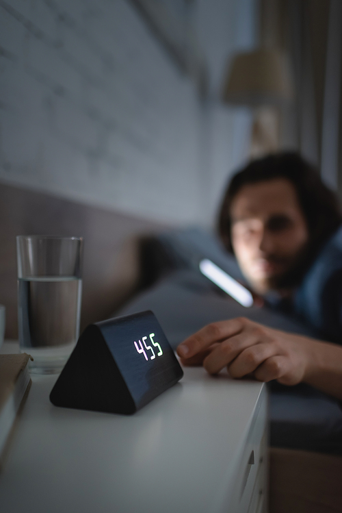 Blurred man touching alarm clock on bedside table at night