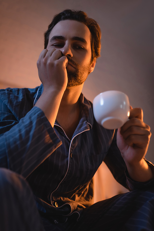 Low angle view of sad man with insomnia holding cup of coffee at home