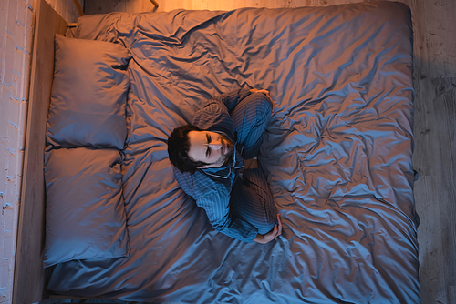 Overhead view of man with sleep disorder sitting with closed eyes on bed