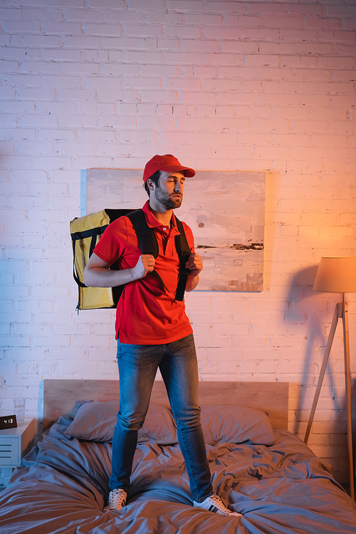 Sleepwalker in uniform holding thermo backpack on bed at night
