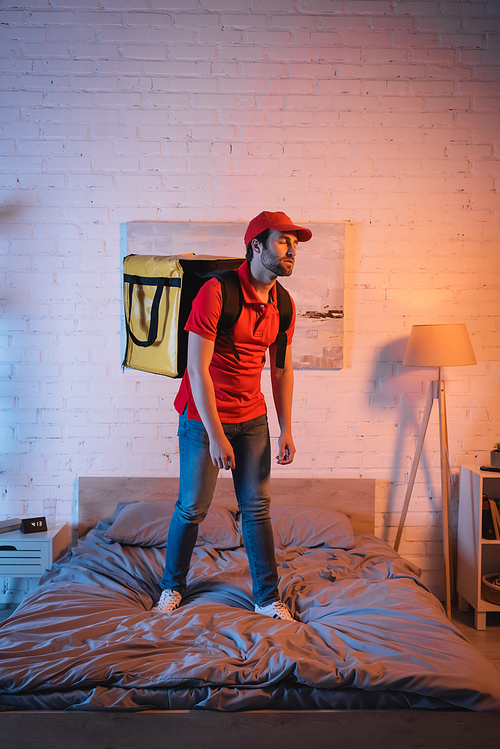 Deliveryman in uniform standing on bed while suffering from sleepwalking at night