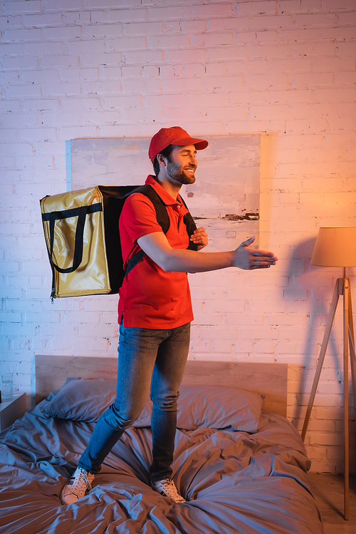 Smiling deliveryman outstretching hand while suffering from sleepwalking on bed