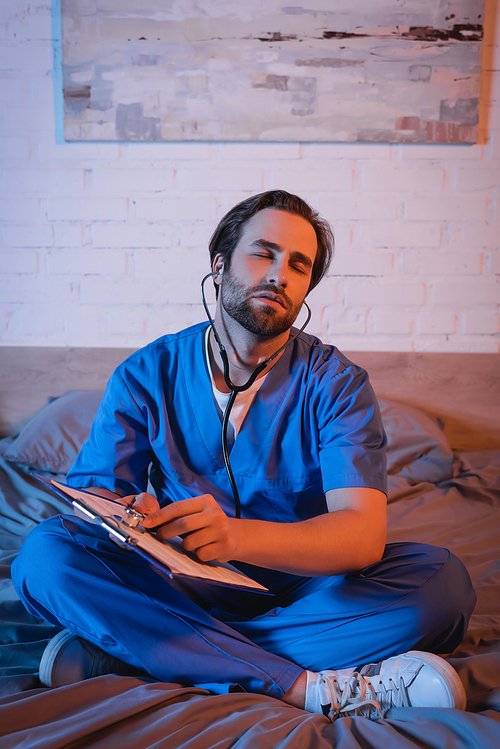 Sleepwalker in doctor uniform and stethoscope pointing at clipboard on bed at night