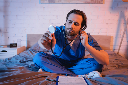 Sleepwalker in doctor uniform holding stethoscope near clipboard on bed at night