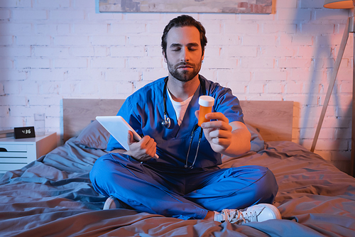 Sleepwalker in doctor uniform holding pills and digital tablet on bed