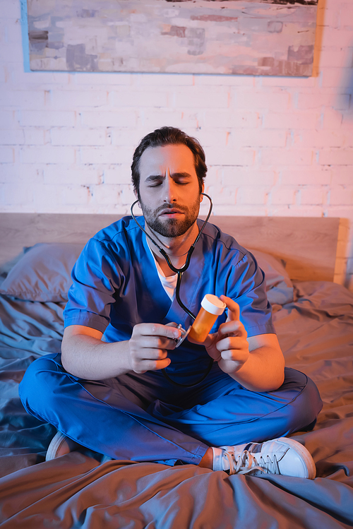 Sleepwalker in doctor uniform holding pills and stethoscope on bed at night