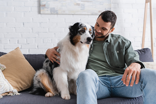 happy bearded man cuddling australian shepherd dog on couch