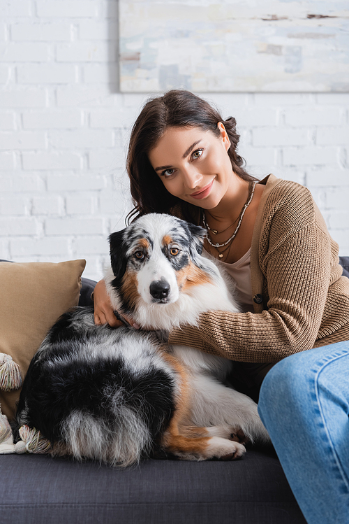 pleased young woman cuddling australian shepherd dog while sitting on couch