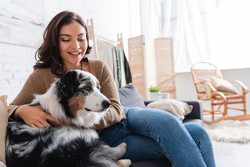 excited young woman cuddling australian shepherd dog while sitting on couch