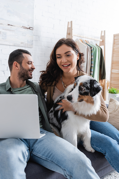 happy young couple watching movie on laptop near australian shepherd dog
