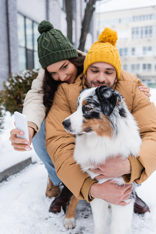 smiling woman in knitted hat taking selfie with boyfriend and australian shepherd dog in winter