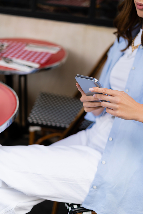 Cropped view of stylish woman using smartphone on terrace of cafe in Paris